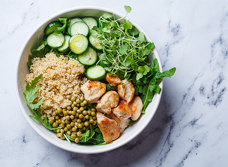 Bowl with grilled chicken, quinoa, peas, cucumbers, greens, and sprouts.