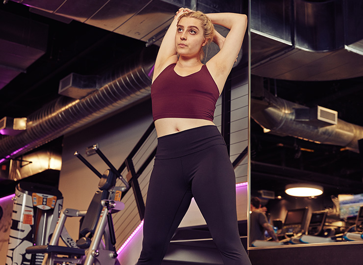 Woman stretching with both arms overhead in the gym.