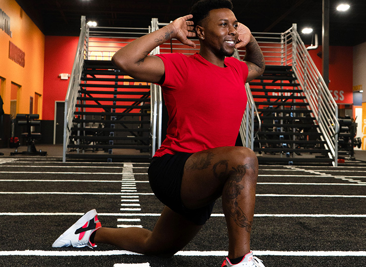 Man doing a kneeling lunge stretch with hands behind his head.