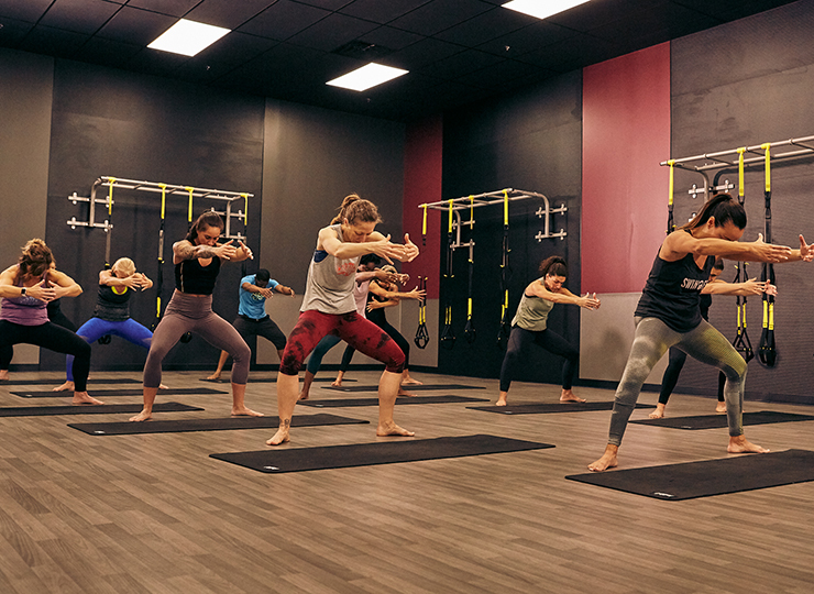 Group fitness class doing squat pulses with arms extended in a studio.