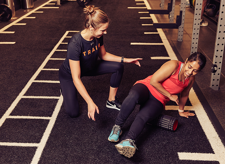 Personal trainer helping a woman foam roll