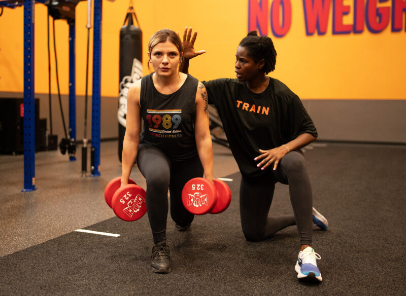 A personal trainer helping a woman with weighted lunges
