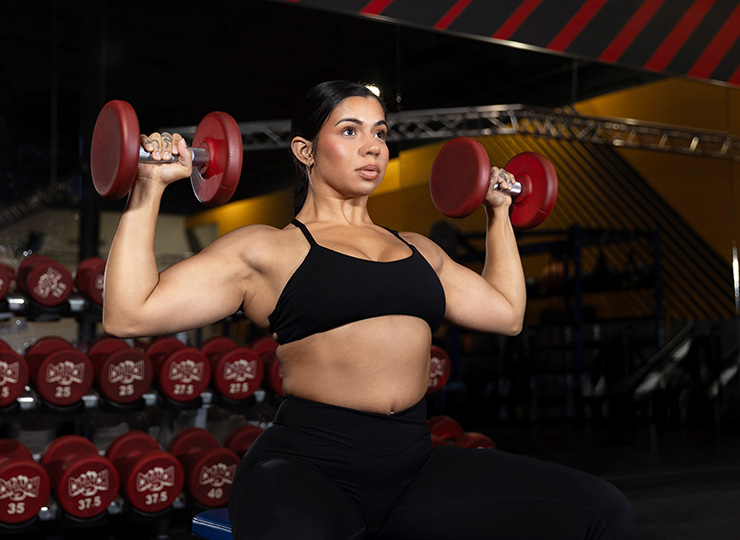 Woman holding dumbbells at shoulder height in a gym.