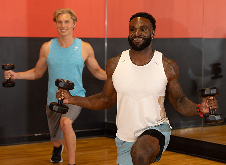 Two men doing dumbbell lunges in a studio.