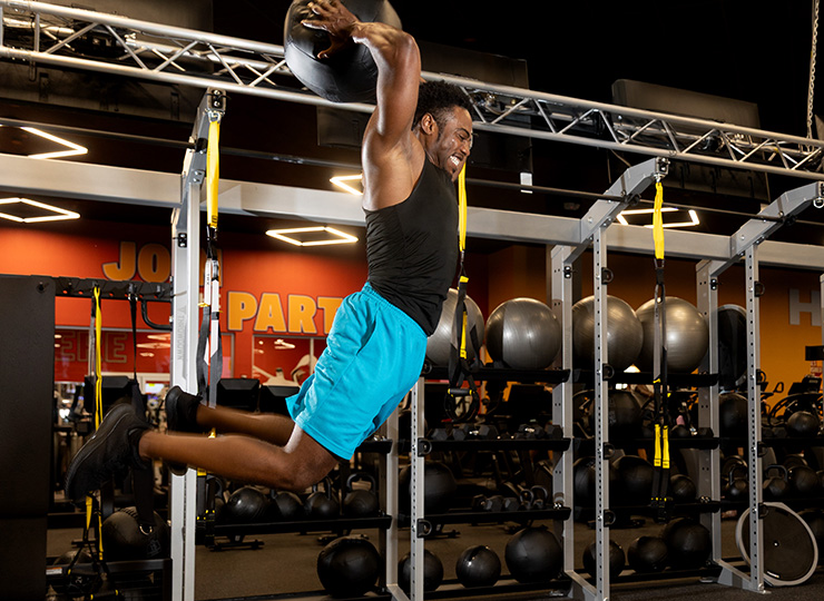 Man jumping with a medicine ball overhead in a gym.